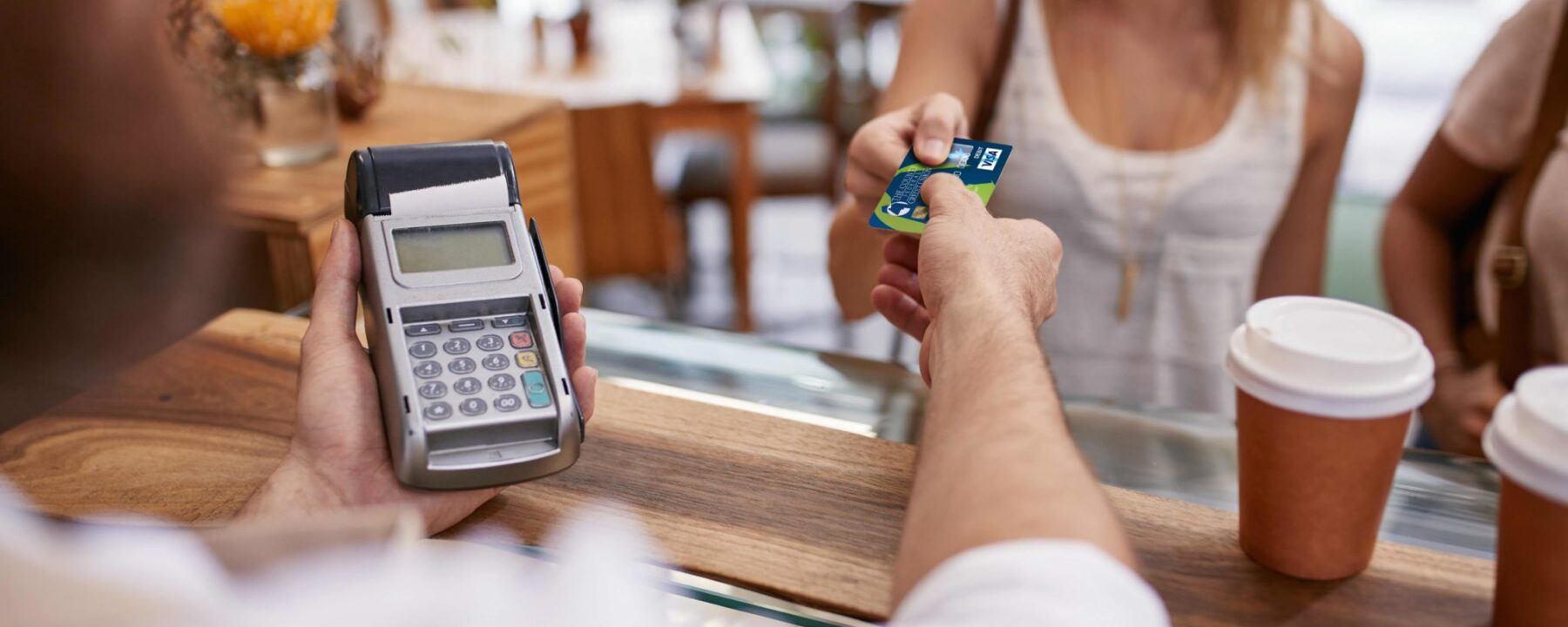 Customer paying for their order with a credit card in a cafe. Bartender holding a credit card reader machine and returning the debit card to female customer after payments.