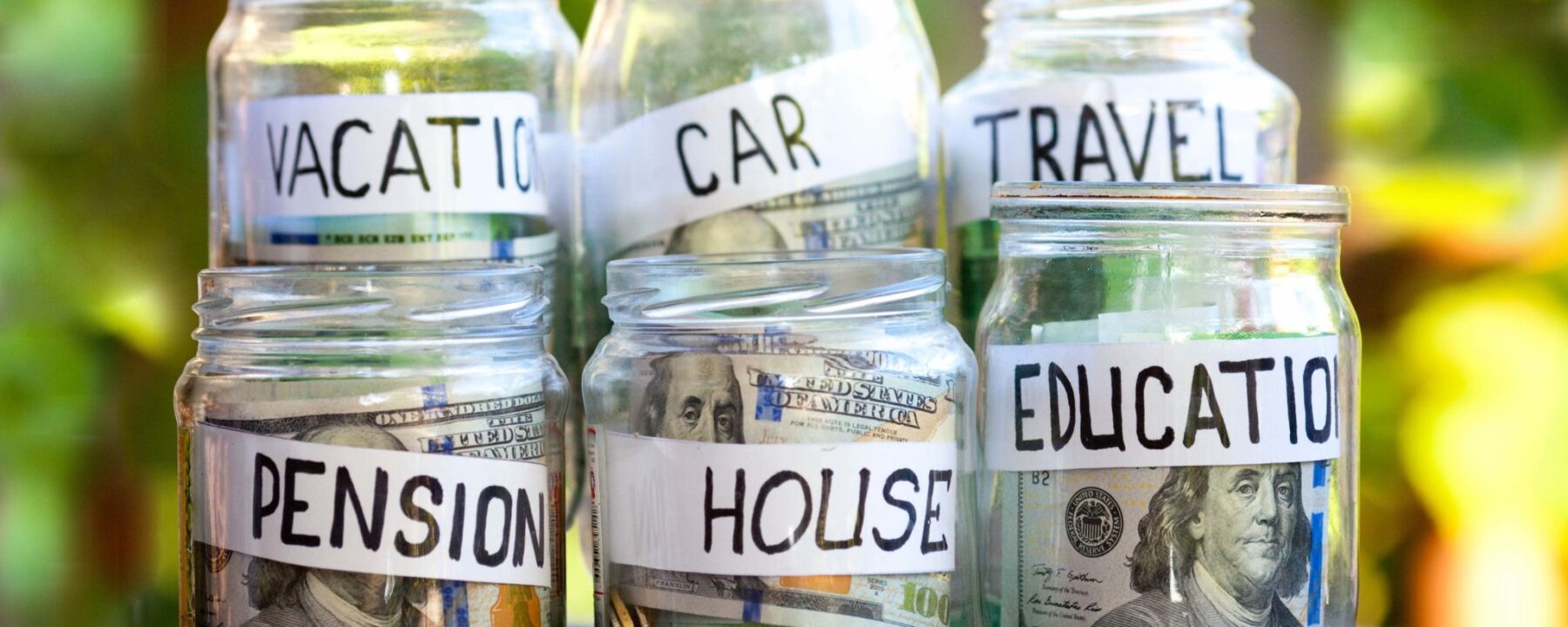 Money jars with money in each with tags that read vacation, car, travel, pension, house and education.